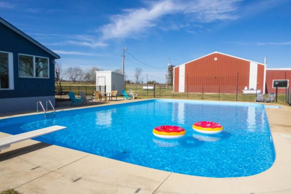 A serene blue pool featuring two colorful inflatables, set against the rustic backdrop of a barn
