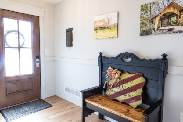 A wooden bench located before a door, with various pictures hanging on the wall in the background