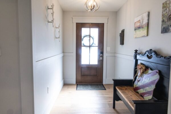 An interior hallway with a wooden bench placed beside the wall, culminating in a door at the opposite end